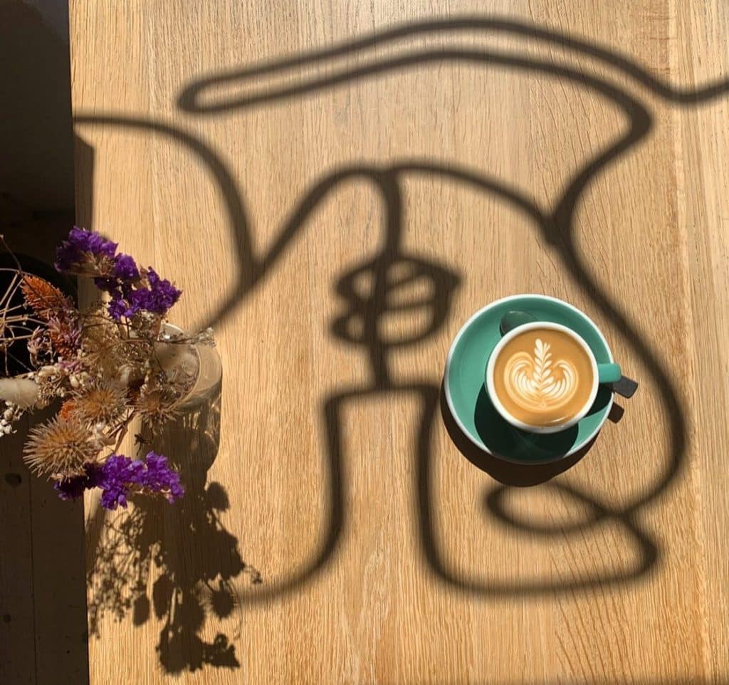 Coffee from Darcy’s Kaffe next to flowers with window reflections